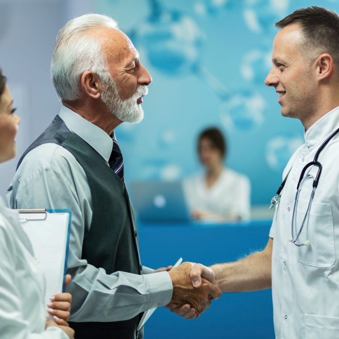 Happy senior businessman and male doctor handshaking while greeting in a hallway at clinic.